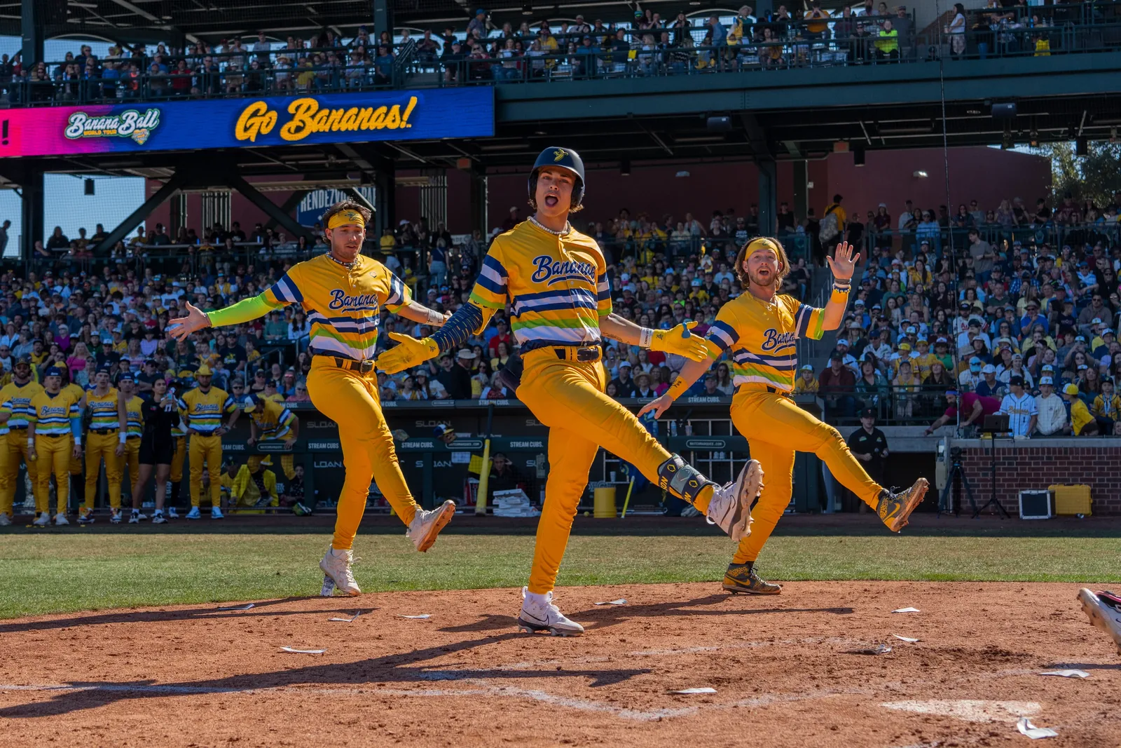 Three Savannah Bananas players performing on the field during a Banana Ball game in Mesa